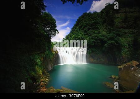 Splendida cascata Shifen nel quartiere di Pingxi, nuova Taipei, circondata da vegetazione lussureggiante, catturata in una giornata estiva nel 2010 con cieli azzurri. Foto Stock