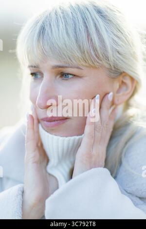 Ritratto ravvicinato di una donna matura triste con i capelli bianchi, che tiene il viso con le mani, soffre di mal di denti o depressione Foto Stock