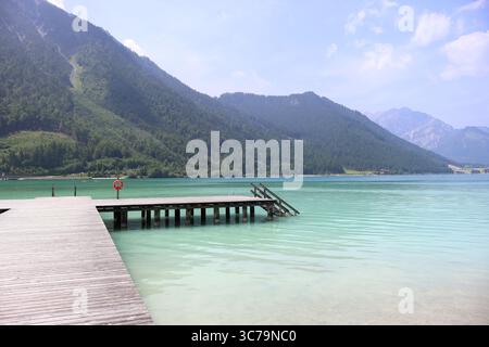 Splendida vista sul lago Achensee in Tirolo, Austria, con un molo in legno che conduce alle calme acque turchesi, circondato da montagne alpine e. Foto Stock