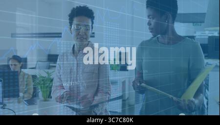 Revisione dei dati sui monitor di due donne aziendali in un ufficio open space, con tablet e cartella gialla Foto Stock