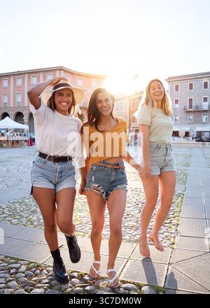 Tre giovani donne che si tengono per mano e camminano in una piazza della città Foto Stock