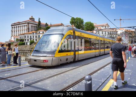 Porto, Portogallo 14 giugno 2025: Un treno Metro do Porto attraversa il famoso ponte Ponte Luís i tra i turisti sul marciapiede Foto Stock