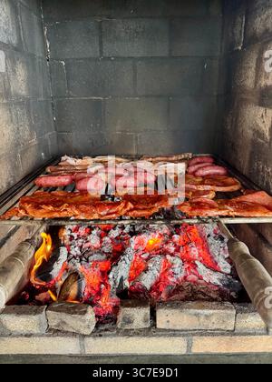 Salsicce e costolette cucinate su carboni caldi accesi su un barbecue. Foto Stock