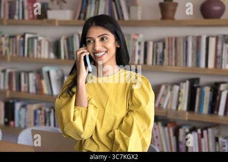 Giovane donna indiana degli anni '25 che si gode una piacevole conversazione su smartphone Foto Stock