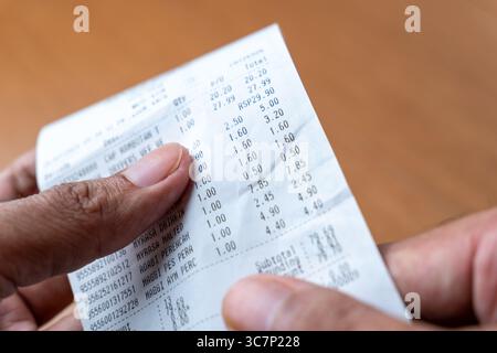 Le mani di una persona stanno reggendo ed esaminando una lunga ricevuta stampata della spesa. Shopping, spese, concetto di budget. Foto Stock