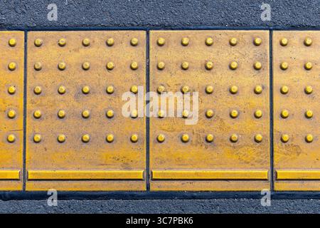 Primo piano di pavimentazione tattile gialla (anche blocchi di tenji, dal nome del braille giapponese) un sistema di indicatori di superficie del terreno testurizzato per aiutare il più piccante Foto Stock