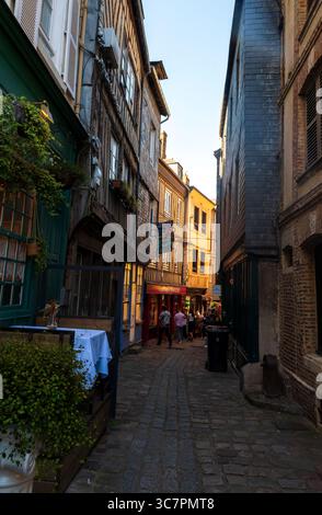 Una stretta strada acciottolata a Honfleur, in Normandia, con edifici in legno e ardesia che catturano l'ultima luce del giorno. Foto Stock