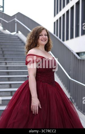 Donna in abito da sera rosso di fronte alle scale, sorridente, da un lato Foto Stock