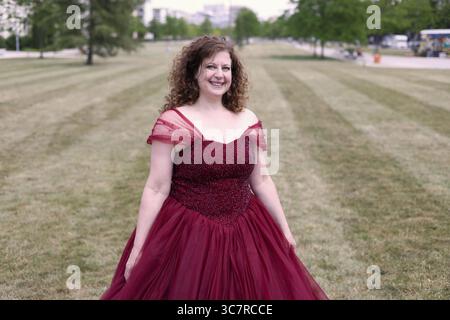 Donna in un pomposo abito da sera rosso su un prato verde, formato paesaggio Foto Stock