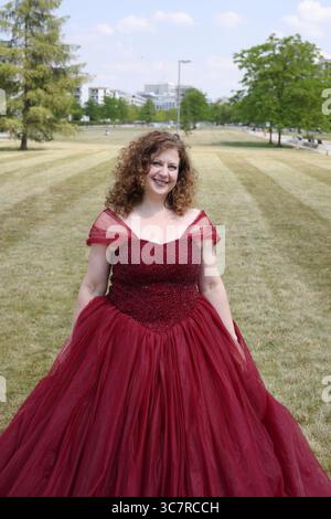 Donna con un pomposo abito da sera rosso su un prato verde, formato ritratto Foto Stock