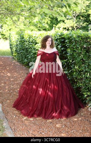 Donna con un pomposo abito da sera rosso davanti a una siepe Foto Stock