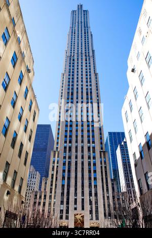 30 Rockefeller Plaza si erge sopra le ali inferiori del Rockefeller Center a Midtown Manhattan, con la sua facciata in pietra calcarea Art Deco adagiata su un cielo azzurro. Foto Stock