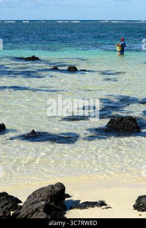 A fisherman wades in shallow turquoise waters with a net basket, Mauritius, April 2010. Foto Stock