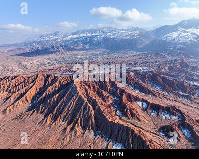 Un ampio giro aereo con drone cattura l'ampio paesaggio rosso del Mars Canyon con le sue formazioni distintive, una città e montagne innevate Foto Stock