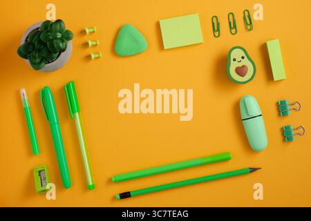 Cornice di penna verde, matita e pennarello su sfondo giallo. Gomma a forma di avocado. In piano. Foto Stock