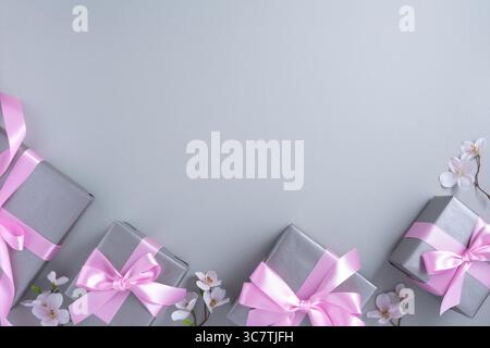 Cornice di scatole regalo grigie con fiocchi e fiori rosa su sfondo grigio chiaro. Presentare il concetto. Flat lay, copyspace. Foto Stock