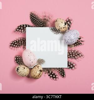 Cornice pasquale composta da uova di quaglia, carta bianca quadrata e piume su sfondo rosa. Layout piatto, vista dall'alto, spazio di copia. Foto Stock