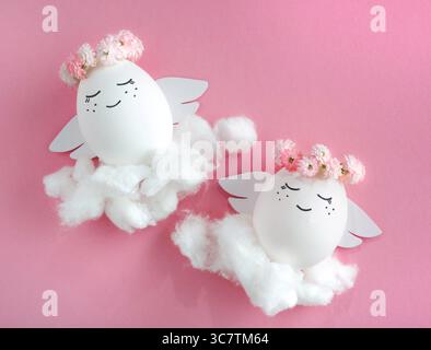 Angelo sorridente fatto di uova in corona di fiori. Uovo di Pasqua. Sfondo rosa. Foto Stock