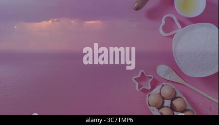 Visualizzazione del mare sotto il cielo viola-rosa e cottura in forno su superficie rosa con recipiente per farina, spazio copia Foto Stock