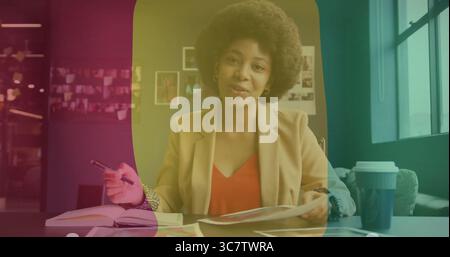 Donna che indossa un blazer beige che esamina documenti nello spazio di lavoro, con penna, notebook e tazza da caffè Foto Stock