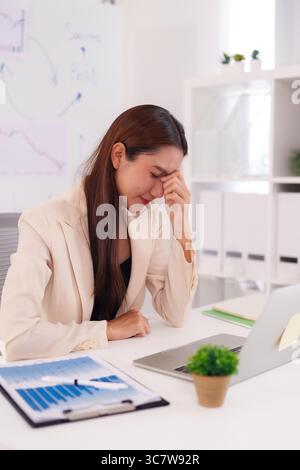 Donna professionale asiatica sopraffatta da difficoltà finanziarie e pressioni aziendali. Le donne adulte sperimentano lo stress del lavoro al des Foto Stock