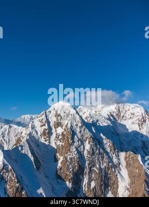 Uno scatto verticale di montagne rocciose e innevate sotto un cielo azzurro e limpido con piccole nuvole in lontananza Foto Stock