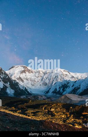 Uno scatto verticale di una vasta catena montuosa innevata con un primo piano roccioso e scuro sotto un bellissimo cielo stellato Foto Stock