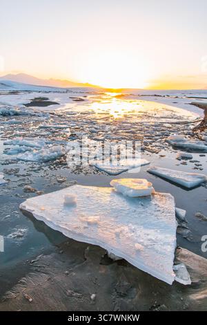 Una foto dall'angolo basso di un lago ghiacciato con grossi frammenti di ghiaccio che galleggiano sull'acqua, con una splendida alba sullo sfondo Foto Stock