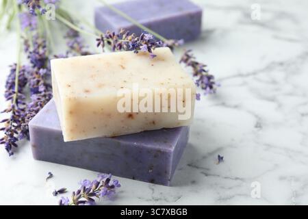 Saponette e fiori di lavanda su un tavolo di marmo bianco, primo piano. Spazio per il testo Foto Stock