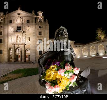 Immagine notturna grandangolare della scultura di Santa Teresa con un mazzo di fiori colorati in primo piano con la Basilica di Santa Teresa in Foto Stock