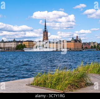 Stoccolma, Svezia - 5 giugno 2025: Una vista panoramica di Stoccolma, Svezia, caratterizzata da edifici colorati lungo il lungomare, un'importante guglia della chiesa, e. Foto Stock