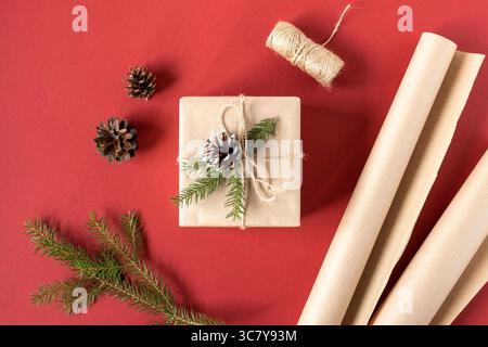 Regali da regalo per Natale e Capodanno. Confezione regalo, carta artigianale, rami e coni di abete rosso su sfondo rosso Foto Stock