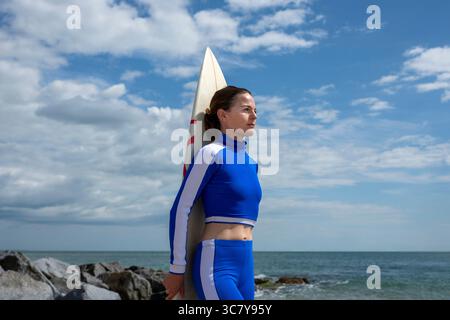 Surfista in muta blu con una tavola da surf in riva all'oceano Foto Stock