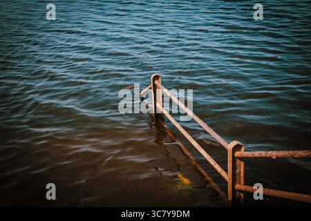 Vista ravvicinata di una ringhiera in metallo arrugginito parzialmente sommersa nel fiume Kukadi a Ozar, Pune, Maharashtra, India. Il colore del cielo si riflette nel fiume. Foto Stock