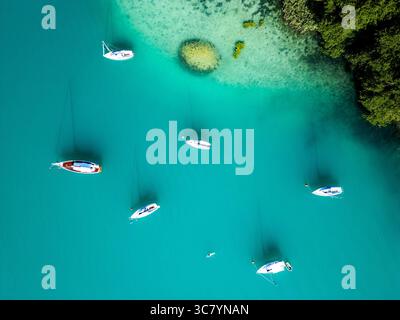 Barche a vela ancorate nelle acque cristalline di Woerthersee, Austria, circondate da una vegetazione lussureggiante Foto Stock