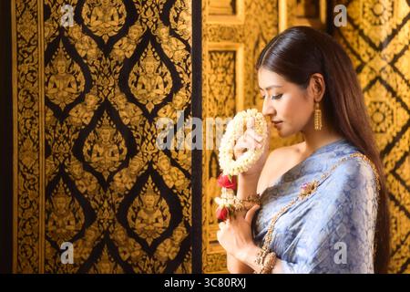 Vista ravvicinata di una giovane donna in abiti tradizionali thailandesi che profuma di ghirlanda floreale (Phuang Malai) Foto Stock