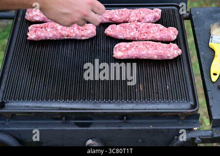 Primo piano di una persona che cucina salsicce su un barbecue all'aperto Foto Stock