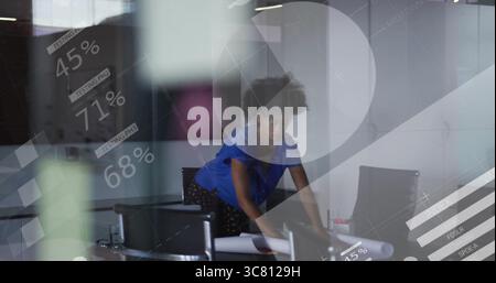 Camicetta blu pendente che esamina i progetti stampati nella sala riunioni, con grafica in vetro Foto Stock