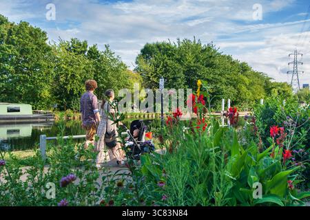 Una giovane coppia con un passeggino che si gode una passeggiata lungo il sentiero cittadino del canale di Lea Valley, vicino alla chiusa di Stonebridge in una serata estiva, Londra, Regno Unito. Foto Stock