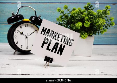 Testo del piano di marketing scritto su carta con sveglia su sfondo in legno Foto Stock