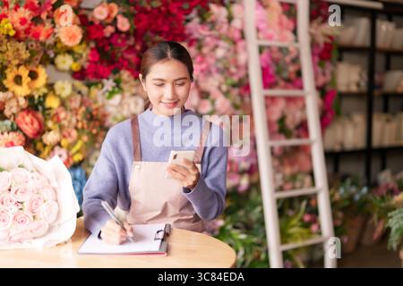 La fiorista asiatica donna adulta gestisce la comunicazione delle operazioni dei negozi di fiori scrive gli ordini dei clienti Foto Stock