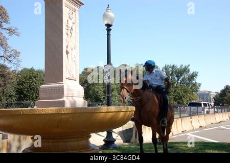 L'ufficiale di polizia a cavallo si ferma vicino a un monumento in pietra e a una fontana a Washington, D.C., sotto cieli limpidi e dintorni urbani Foto Stock