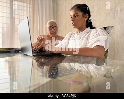Nipote indiana che insegna alle donne anziane (nonna) a utilizzare il laptop a casa. Lavorare insieme per l'assegnazione scolastica utilizzando un laptop. Foto Stock