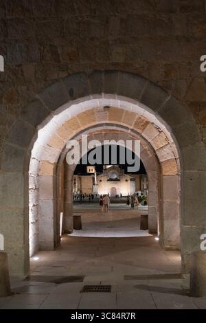 Chiesa di San Pedro Apostolo vista attraverso l'arco della porta dell'alcazar delle mura di Avila, in un'immagine notturna con alcuni turisti che passeggiano Foto Stock