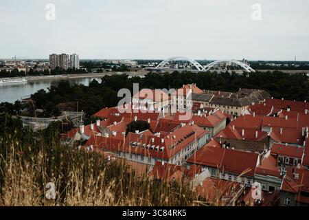 Vista sopraelevata di Novi Sad con tetti rossi di Petrovaradin e moderni edifici sul Danubio. Foto Stock
