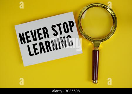 Non smettere mai di imparare testo scritto su carta con lente d'ingrandimento Foto Stock