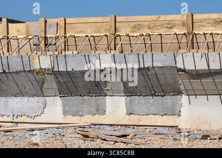 Una vista dettagliata di un ponte mostra forme in cemento, barre di rinforzo in acciaio esposte e casseforme in legno sotto la luce solare intensa, evidenziando la fase iniziale Foto Stock