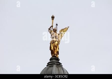 Una statua dorata di una figura femminile alata che regge una torcia si erge in modo prominente sulla cupola di un edificio, rappresentando la vittoria e la grandiosità contro Foto Stock