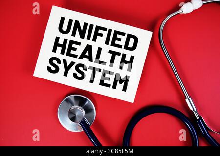 Sistema sanitario unificato testo scritto su carta con stetoscopio su sfondo rosso Foto Stock