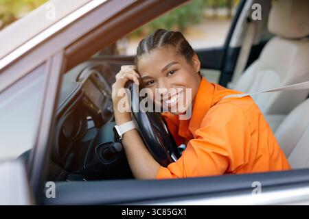 Affascinante donna nera che riposa sul volante con un grande sorriso Foto Stock